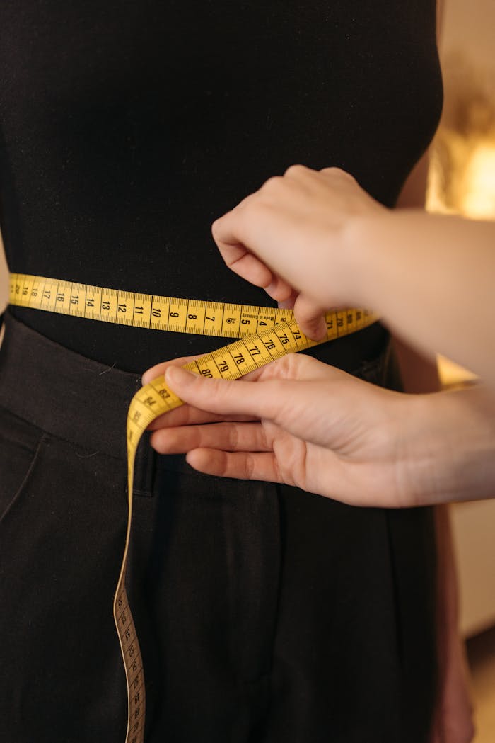 Close-up of a fashion designer measuring a clients waist using a yellow tape in an indoor workshop.
